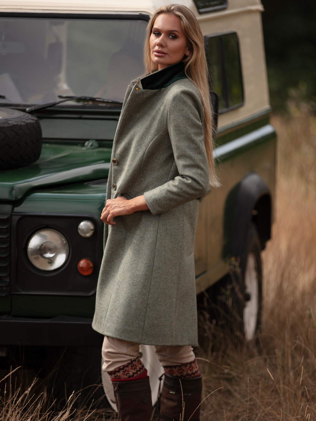 Lichfield Long Ladies' Tweed Coat in pastel green herringbone wool with John Partridge branded buttons, soft satin turquoise lining, forest green velvet cuffs and under collar, and reversible back belt. Features include 2 front pockets, back vent, and knee-length design. Available in pastel green, pink, and blue. Made in England.