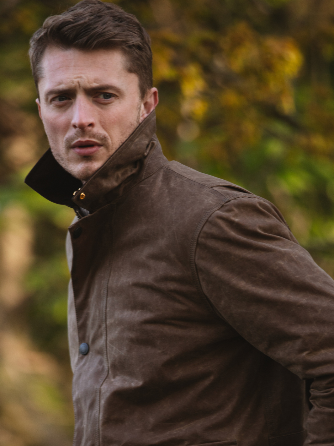Hinterland Jacket in heavy tan waxed cotton with a desert finish, featuring a hip-length design, oversized fit, quilted brown lining, dark brown moleskin trims, and antique brass plate. Includes 2 front pockets, zipped pocket, inner wallet pocket, and YKK zip with storm flap. Limited edition, part of Partridge England's range.