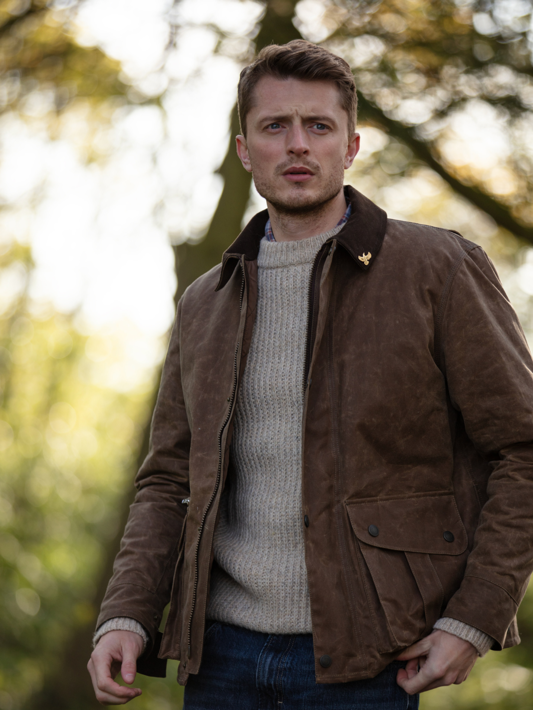 Hinterland Jacket in heavy tan waxed cotton with a desert finish, featuring a hip-length design, oversized fit, quilted brown lining, dark brown moleskin trims, and antique brass plate. Includes 2 front pockets, zipped pocket, inner wallet pocket, and YKK zip with storm flap. Limited edition, part of Partridge England's range.