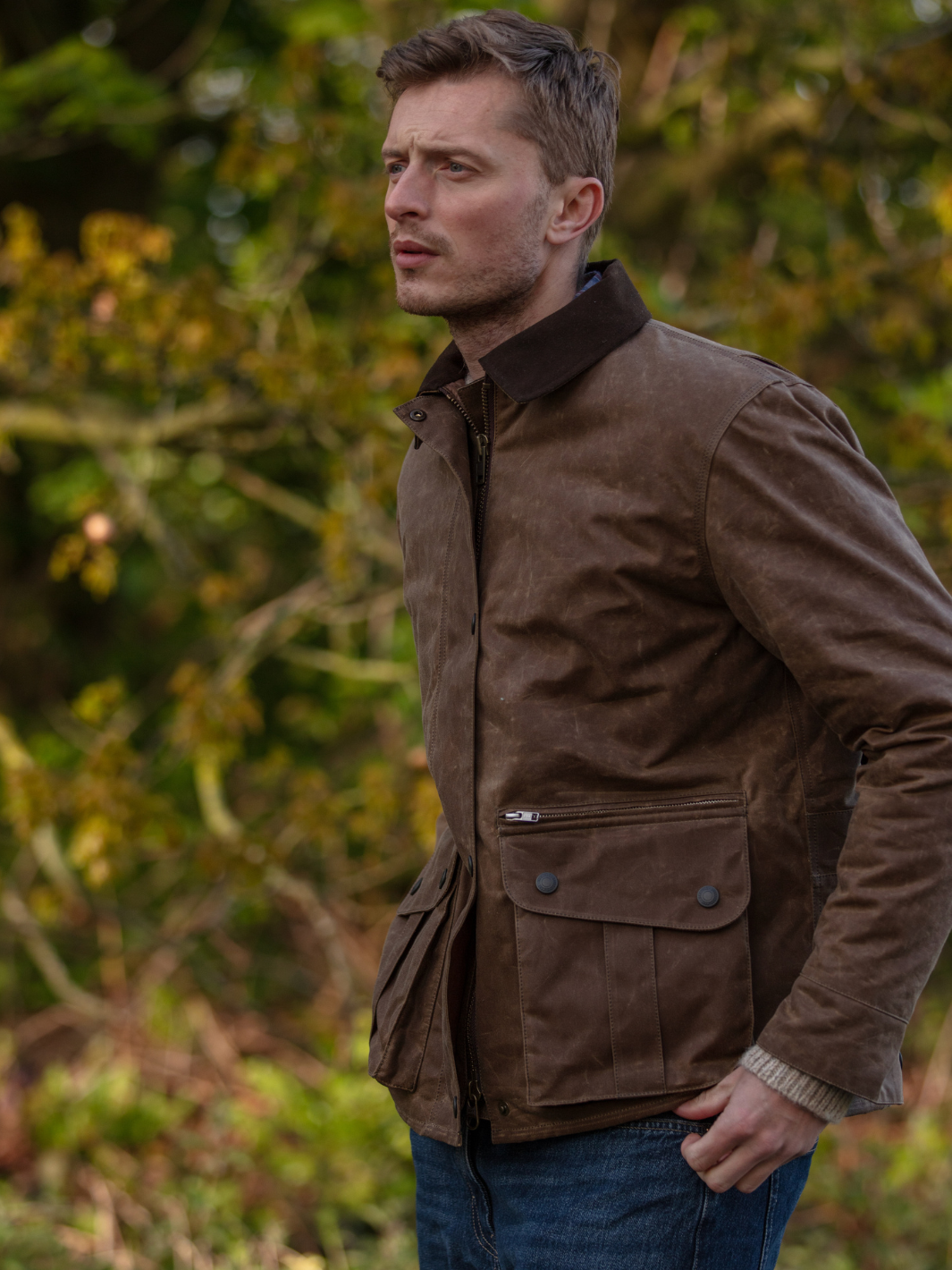 Hinterland Jacket in heavy tan waxed cotton with a desert finish, featuring a hip-length design, oversized fit, quilted brown lining, dark brown moleskin trims, and antique brass plate. Includes 2 front pockets, zipped pocket, inner wallet pocket, and YKK zip with storm flap. Limited edition, part of Partridge England's range.