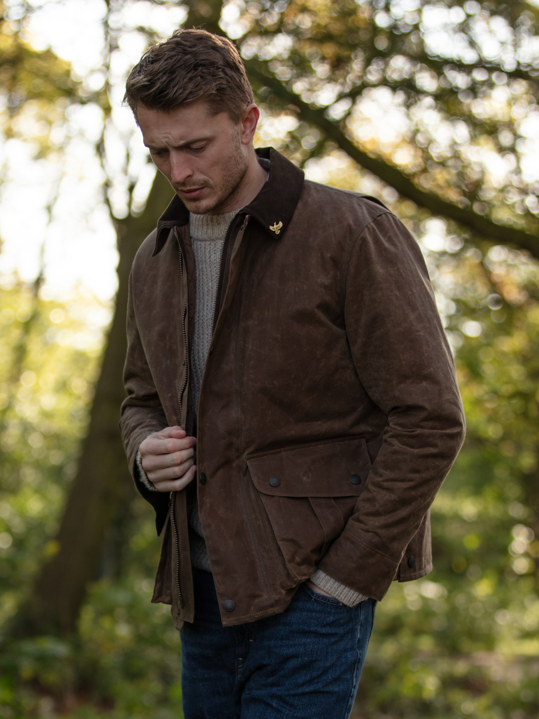 Hinterland Jacket in heavy tan waxed cotton with a desert finish, featuring a hip-length design, oversized fit, quilted brown lining, dark brown moleskin trims, and antique brass plate. Includes 2 front pockets, zipped pocket, inner wallet pocket, and YKK zip with storm flap. Limited edition, part of Partridge England's range.