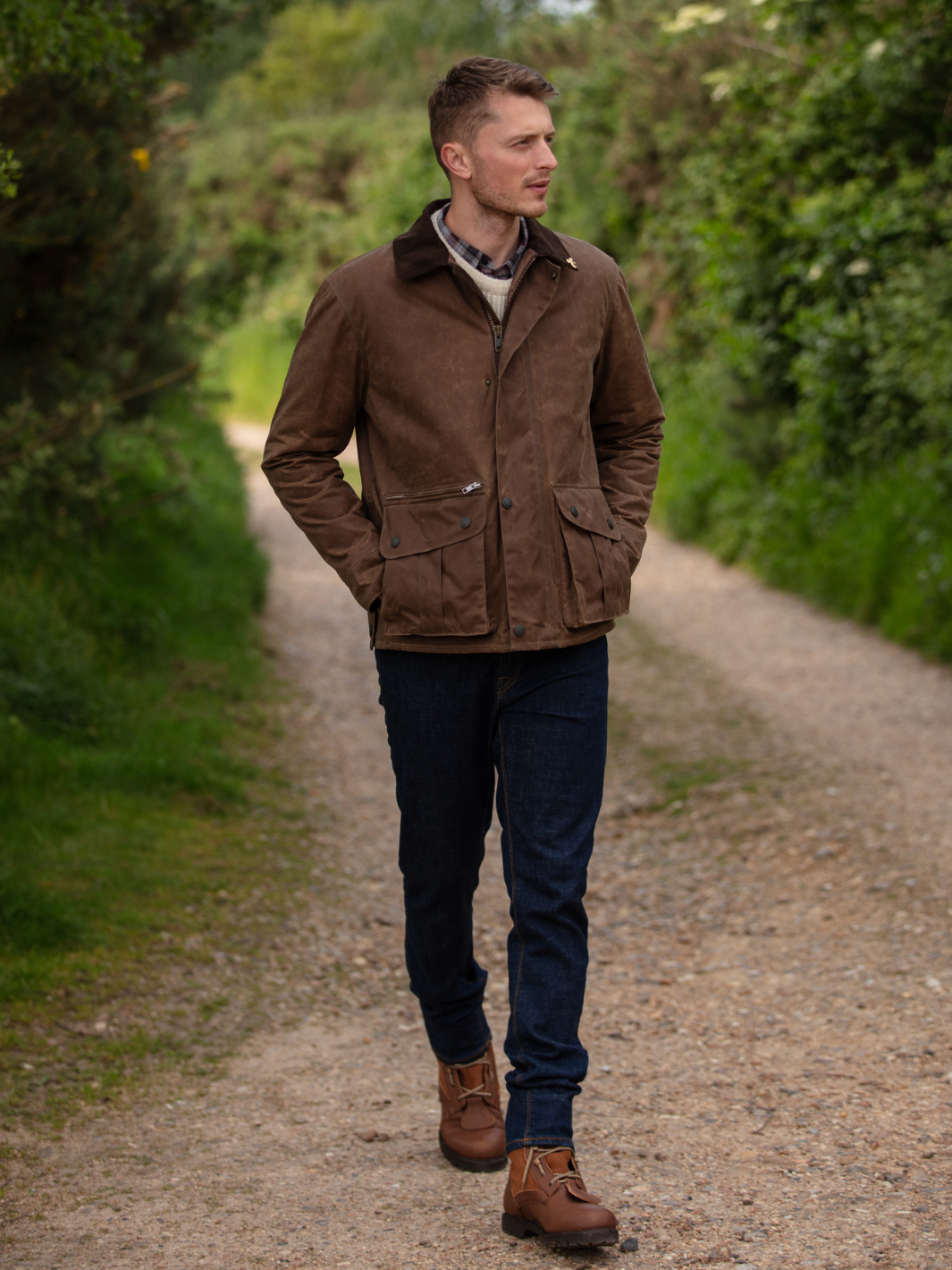 Hinterland Jacket in heavy tan waxed cotton with a desert finish, featuring a hip-length design, oversized fit, quilted brown lining, dark brown moleskin trims, and antique brass plate. Includes 2 front pockets, zipped pocket, inner wallet pocket, and YKK zip with storm flap. Limited edition, part of Partridge England's range.