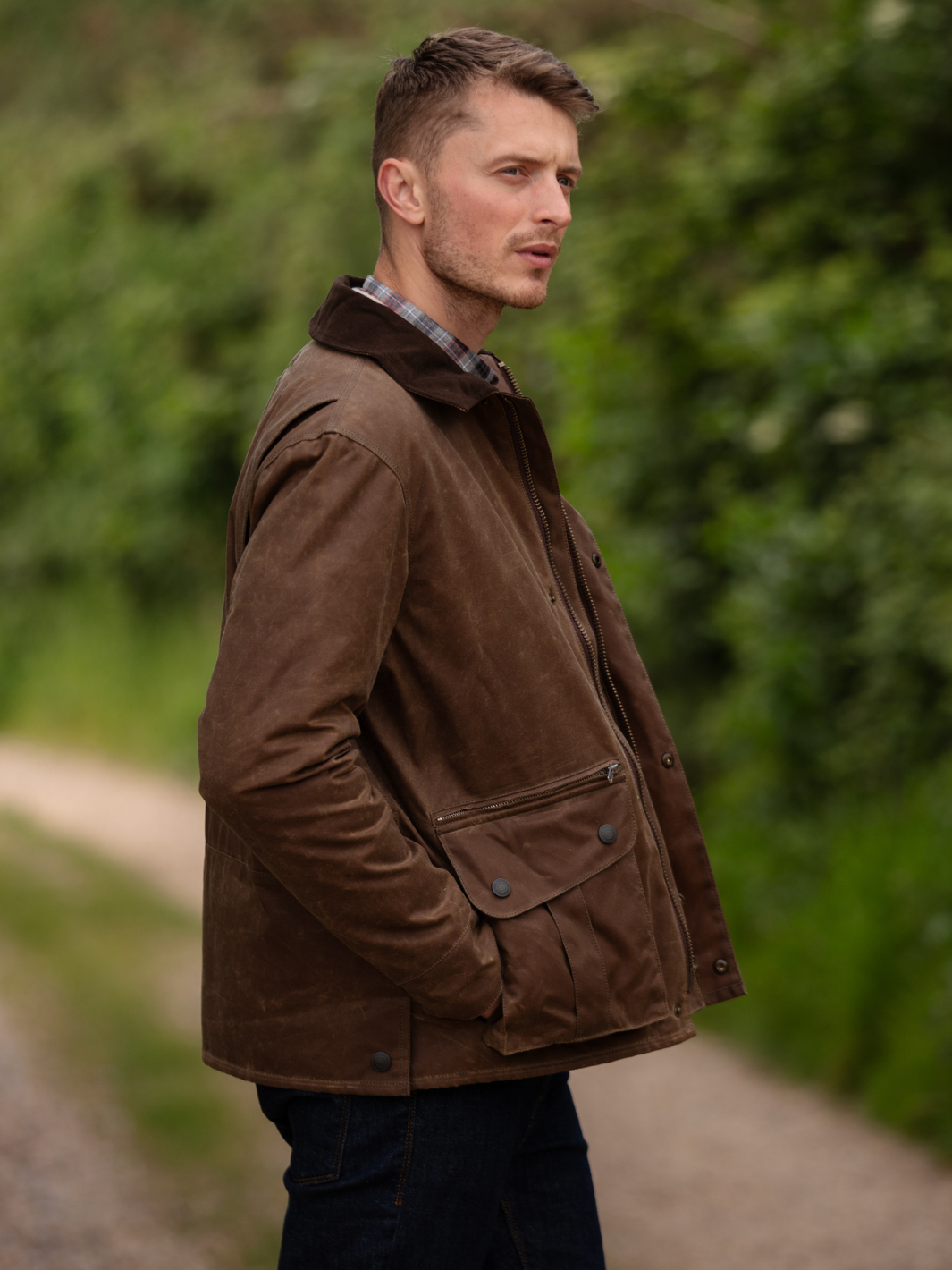 Hinterland Jacket in heavy tan waxed cotton with a desert finish, featuring a hip-length design, oversized fit, quilted brown lining, dark brown moleskin trims, and antique brass plate. Includes 2 front pockets, zipped pocket, inner wallet pocket, and YKK zip with storm flap. Limited edition, part of Partridge England's range.