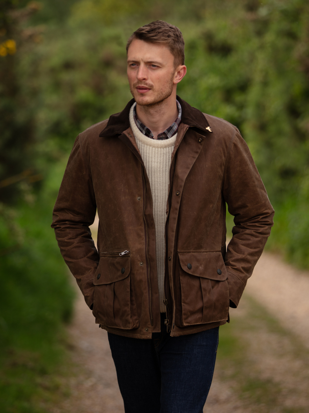Hinterland Jacket in heavy tan waxed cotton with a desert finish, featuring a hip-length design, oversized fit, quilted brown lining, dark brown moleskin trims, and antique brass plate. Includes 2 front pockets, zipped pocket, inner wallet pocket, and YKK zip with storm flap. Limited edition, part of Partridge England's range.