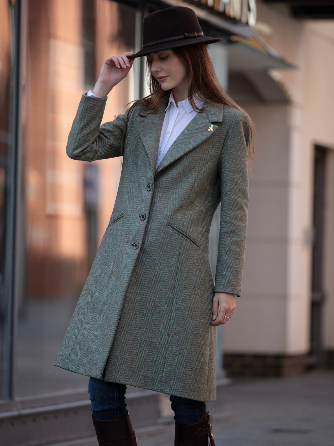 Lichfield Long Ladies' Tweed Coat in pastel green herringbone wool with John Partridge branded buttons, soft satin turquoise lining, forest green velvet cuffs and under collar, and reversible back belt. Features include 2 front pockets, back vent, and knee-length design. Available in pastel green, pink, and blue. Made in England.