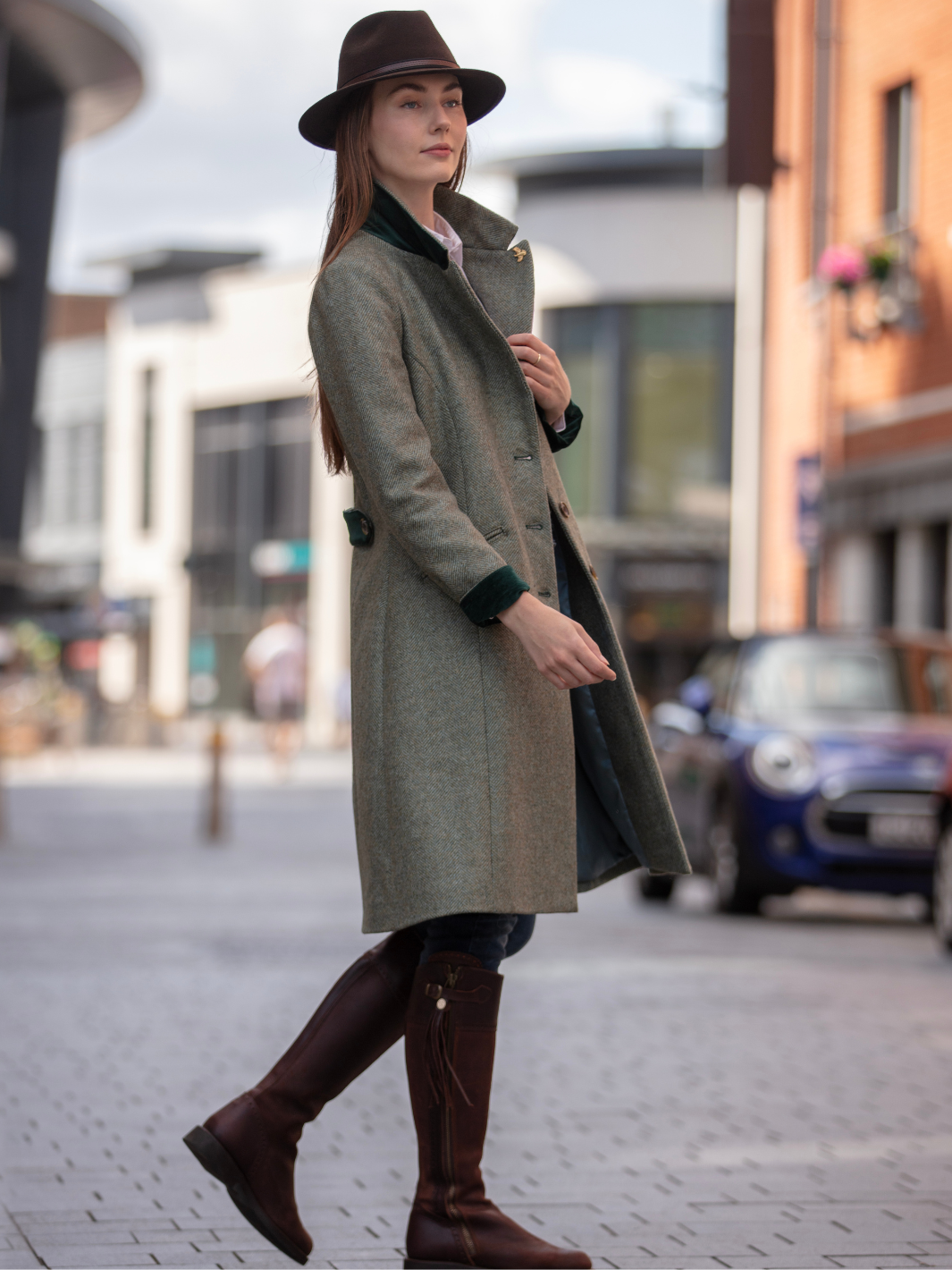 Lichfield Long Ladies' Tweed Coat in pastel green herringbone wool with John Partridge branded buttons, soft satin turquoise lining, forest green velvet cuffs and under collar, and reversible back belt. Features include 2 front pockets, back vent, and knee-length design. Available in pastel green, pink, and blue. Made in England.