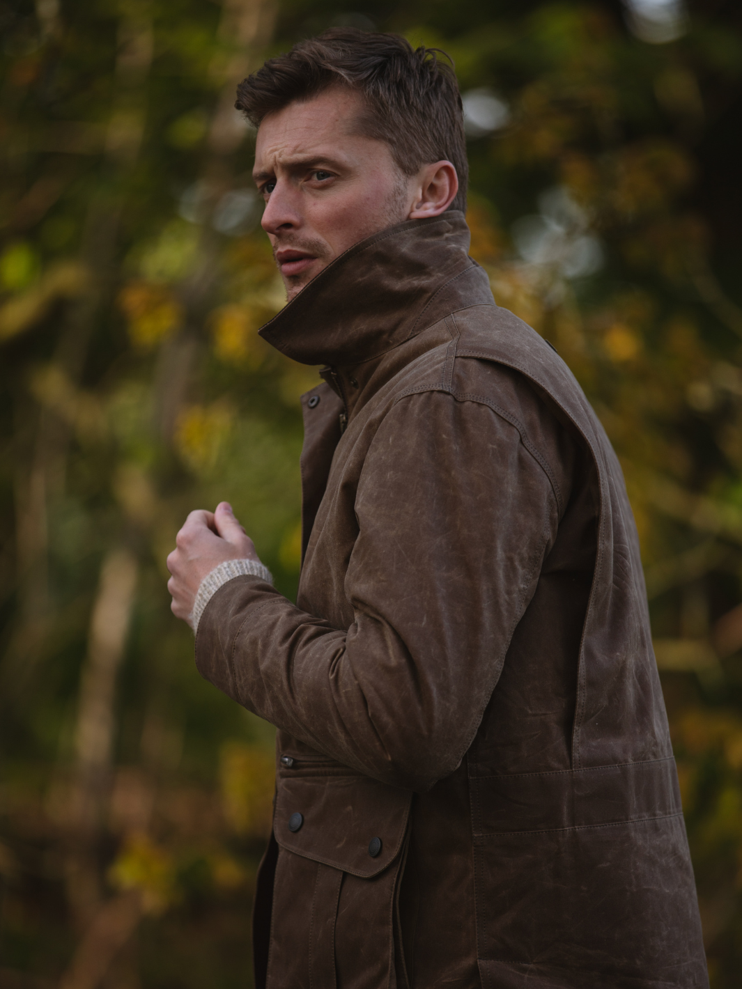 Hinterland Jacket in heavy tan waxed cotton with a desert finish, featuring a hip-length design, oversized fit, quilted brown lining, dark brown moleskin trims, and antique brass plate. Includes 2 front pockets, zipped pocket, inner wallet pocket, and YKK zip with storm flap. Limited edition, part of Partridge England's range.