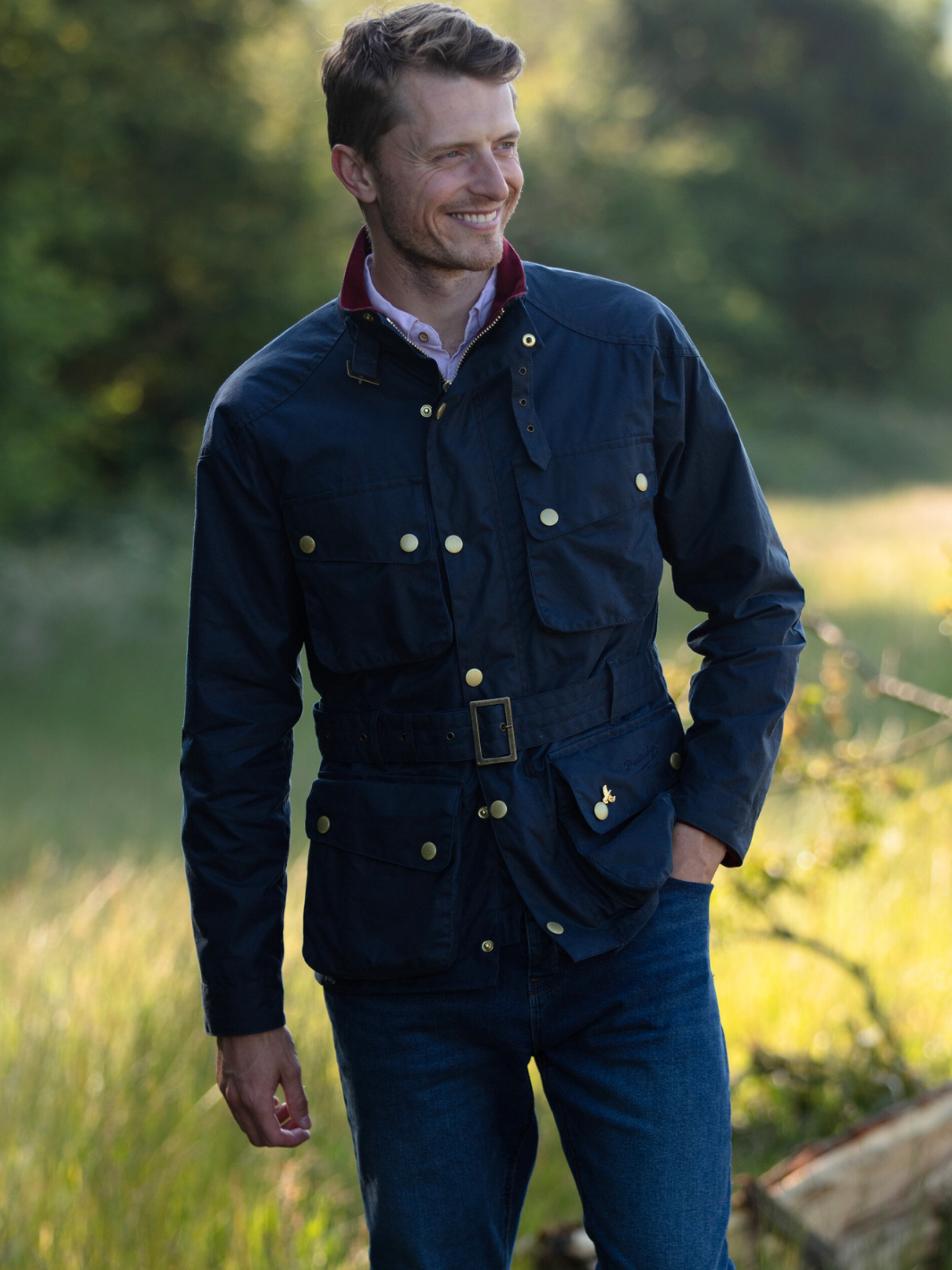 Men's Wax Biker Jacket in Ocean Navy with cherry check lining, burgundy cotton moleskin collar, oversized pockets, and detachable belt. Crafted from British waxed material with tonal embroidery and gold-coloured studs for a blend of tradition, luxury, and modern function.