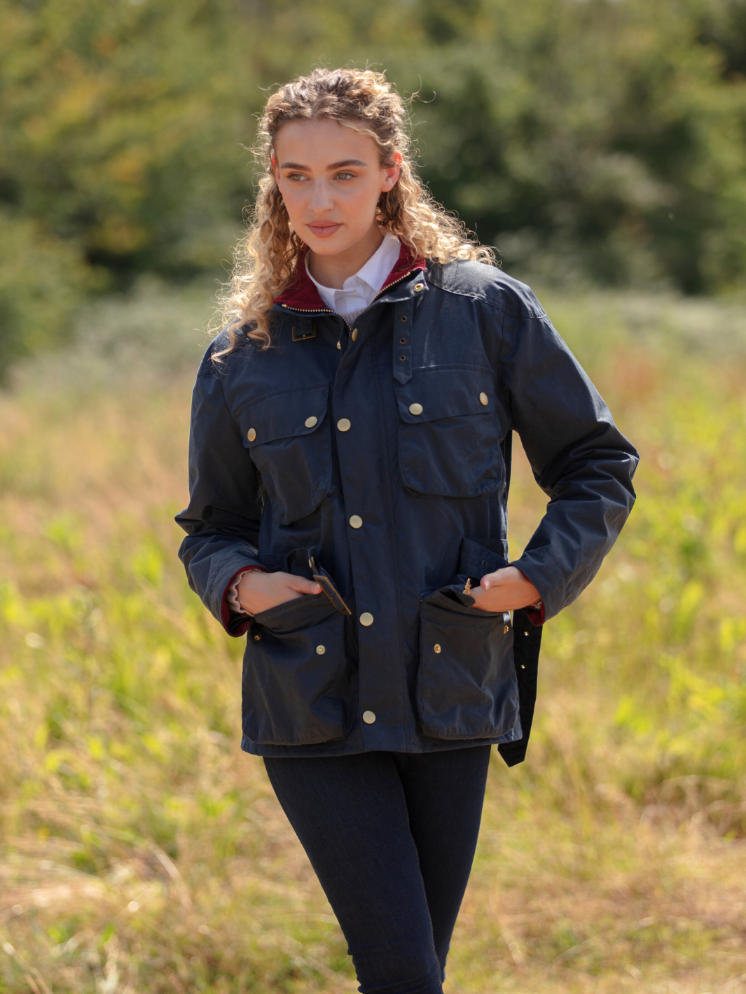 Wax Biker Jacket in Ocean Navy with cherry check lining, burgundy cotton moleskin collar, oversized pockets, and detachable belt. Crafted from British waxed material with tonal embroidery and gold-coloured studs for a blend of tradition, luxury, and modern function.