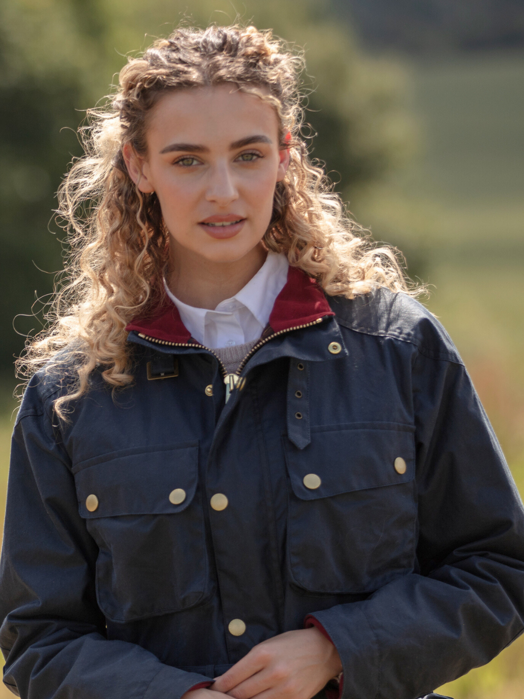 Wax Biker Jacket in Ocean Navy with cherry check lining, burgundy cotton moleskin collar, oversized pockets, and detachable belt. Crafted from British waxed material with tonal embroidery and gold-coloured studs for a blend of tradition, luxury, and modern function.