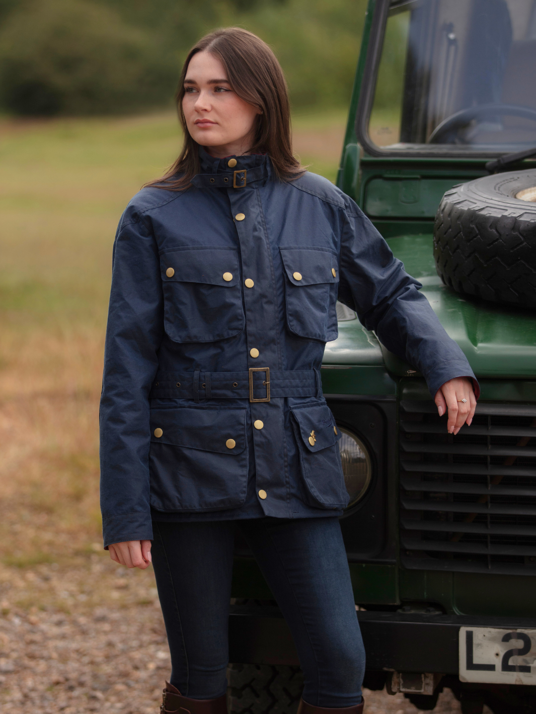 Wax Biker Jacket in Ocean Navy with cherry check lining, burgundy cotton moleskin collar, oversized pockets, and detachable belt. Crafted from British waxed material with tonal embroidery and gold-coloured studs for a blend of tradition, luxury, and modern function.