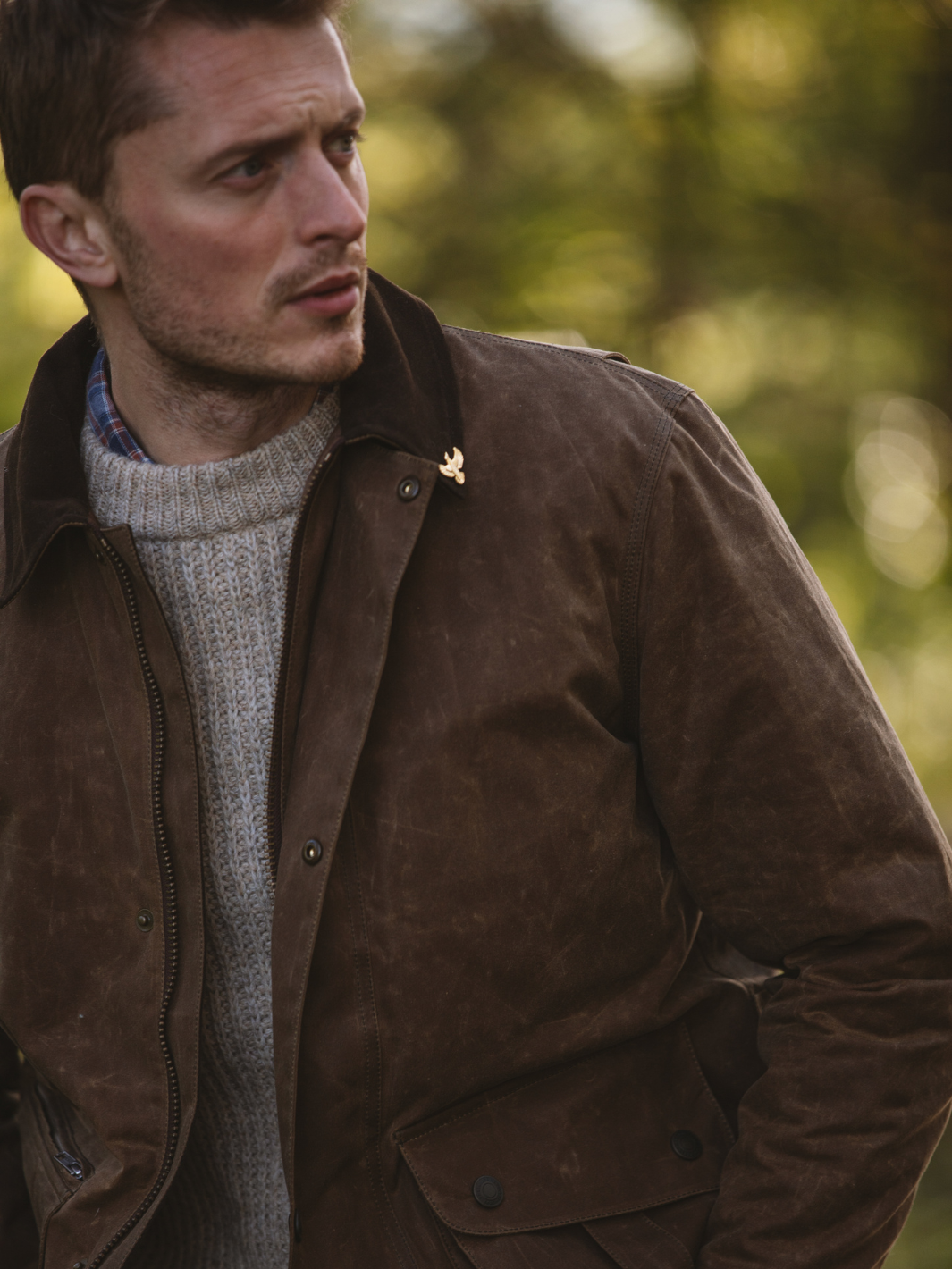 Hinterland Jacket in heavy tan waxed cotton with a desert finish, featuring a hip-length design, oversized fit, quilted brown lining, dark brown moleskin trims, and antique brass plate. Includes 2 front pockets, zipped pocket, inner wallet pocket, and YKK zip with storm flap. Limited edition, part of Partridge England's range.
