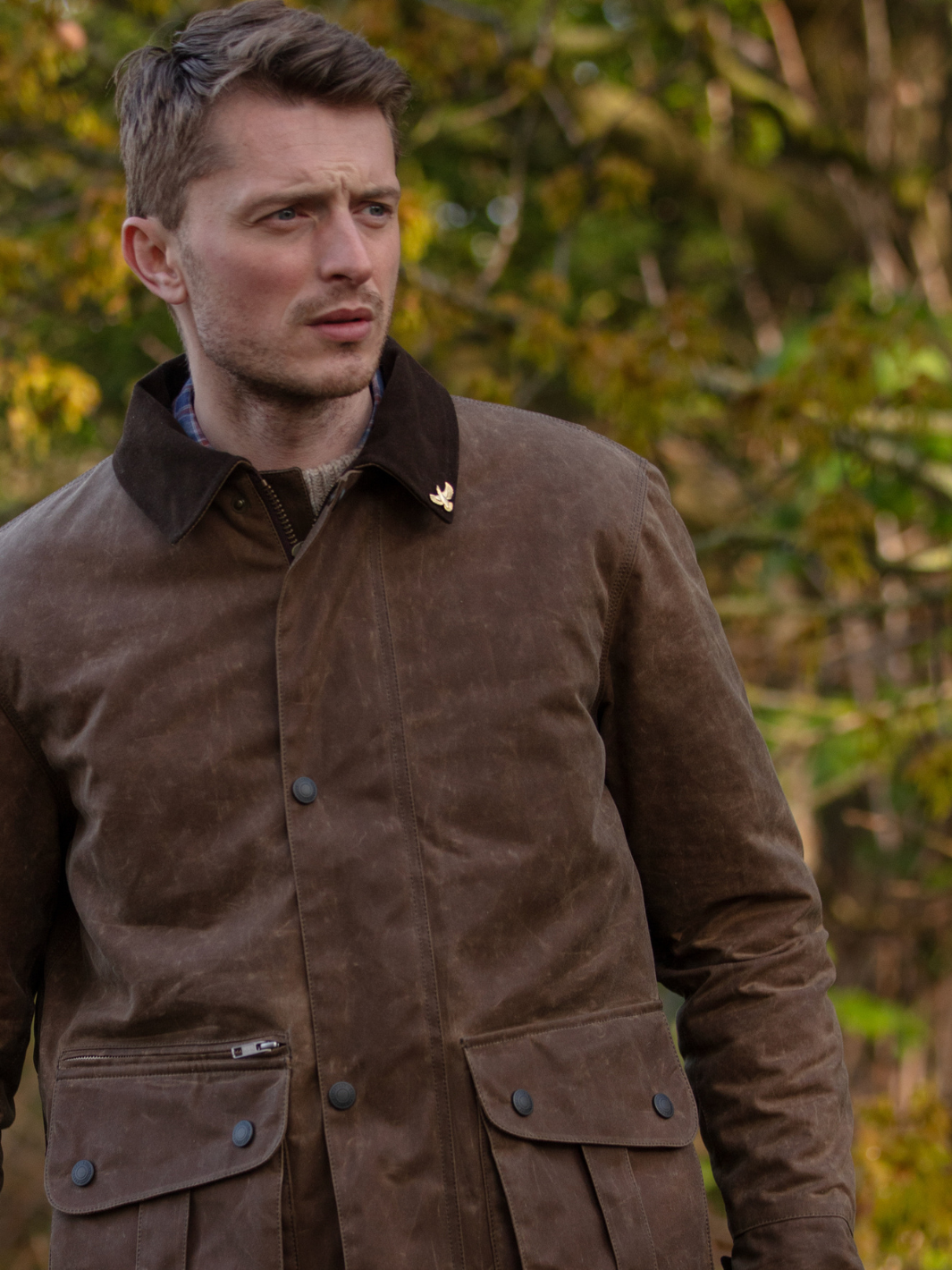Hinterland Jacket in heavy tan waxed cotton with a desert finish, featuring a hip-length design, oversized fit, quilted brown lining, dark brown moleskin trims, and antique brass plate. Includes 2 front pockets, zipped pocket, inner wallet pocket, and YKK zip with storm flap. Limited edition, part of Partridge England's range.