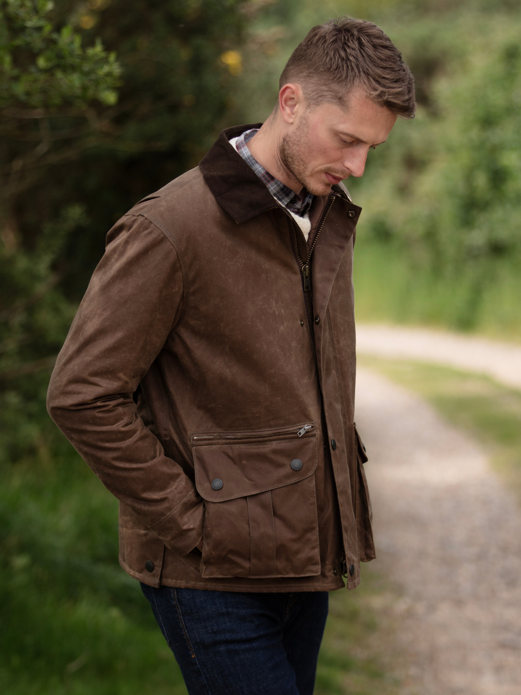 Hinterland Jacket in heavy tan waxed cotton with a desert finish, featuring a hip-length design, oversized fit, quilted brown lining, dark brown moleskin trims, and antique brass plate. Includes 2 front pockets, zipped pocket, inner wallet pocket, and YKK zip with storm flap. Limited edition, part of Partridge England's range.