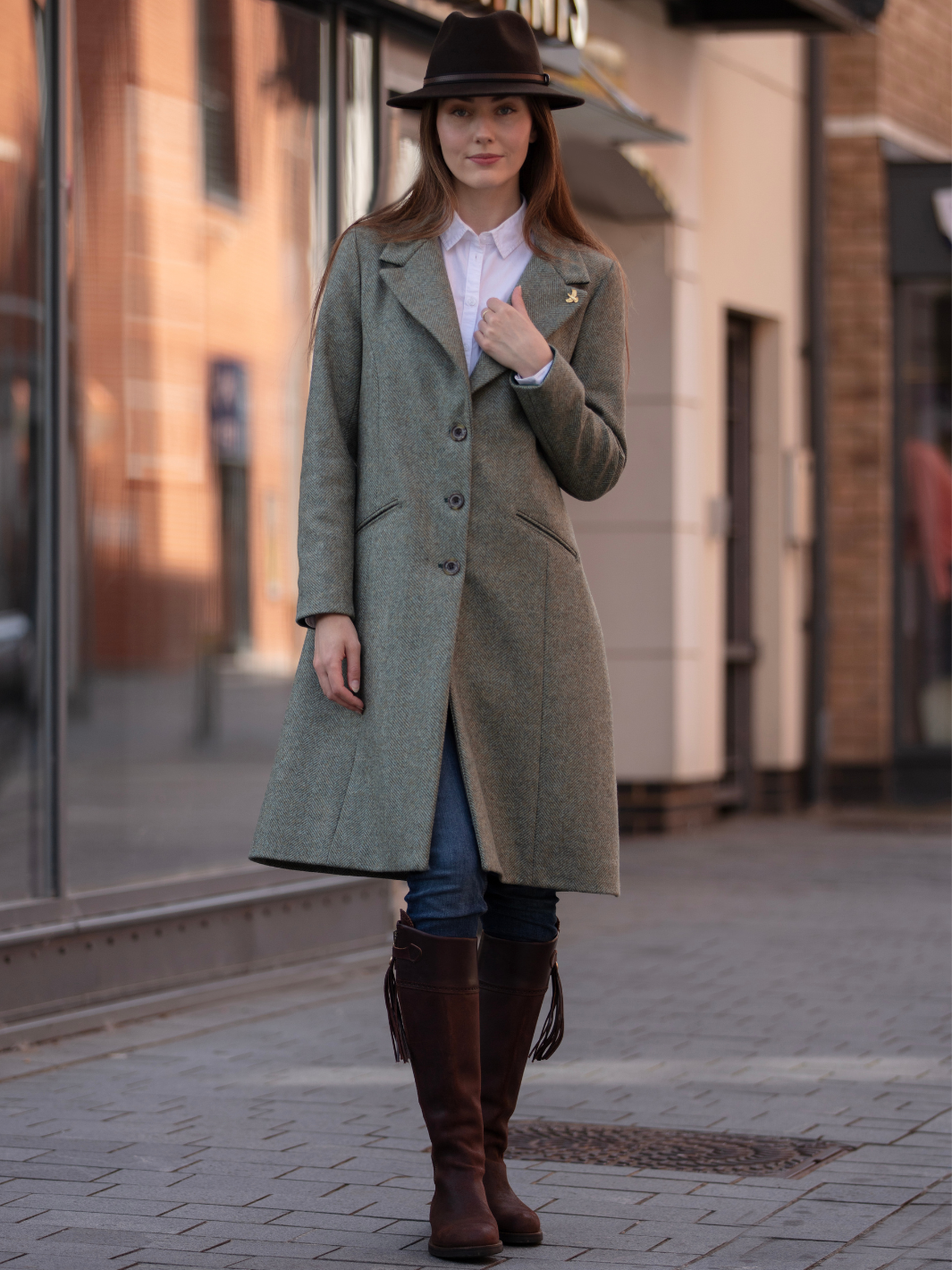 Lichfield Long Ladies' Tweed Coat in pastel green herringbone wool with John Partridge branded buttons, soft satin turquoise lining, forest green velvet cuffs and under collar, and reversible back belt. Features include 2 front pockets, back vent, and knee-length design. Available in pastel green, pink, and blue. Made in England.