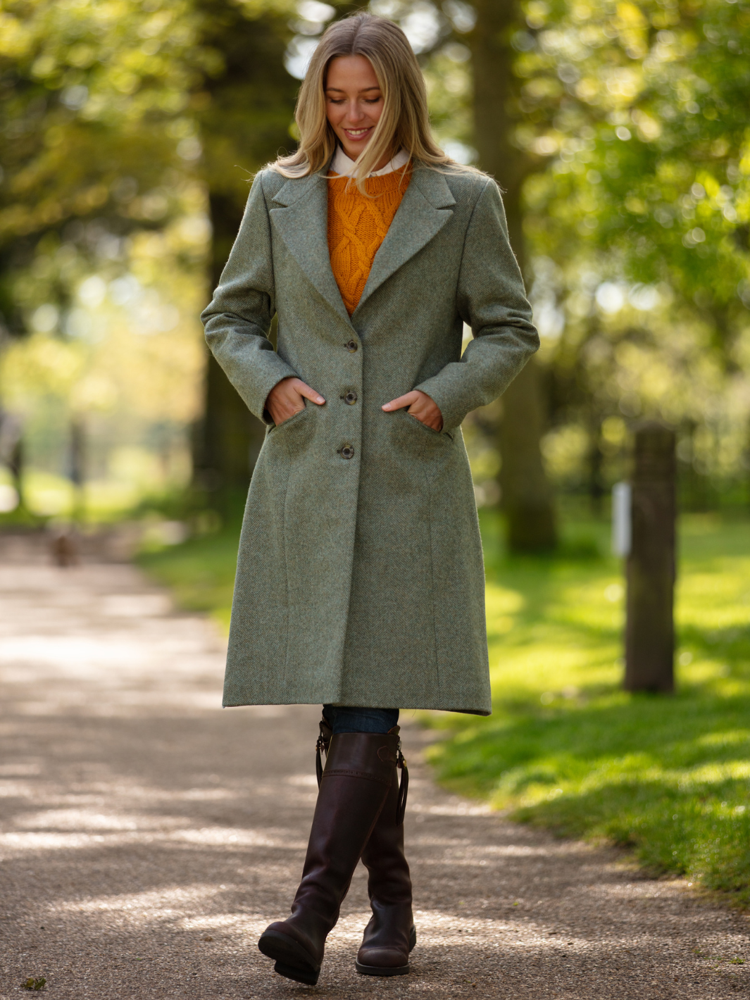 Lichfield Long Ladies' Tweed Coat in pastel green herringbone wool with John Partridge branded buttons, soft satin turquoise lining, forest green velvet cuffs and under collar, and reversible back belt. Features include 2 front pockets, back vent, and knee-length design. Available in pastel green, pink, and blue. Made in England.