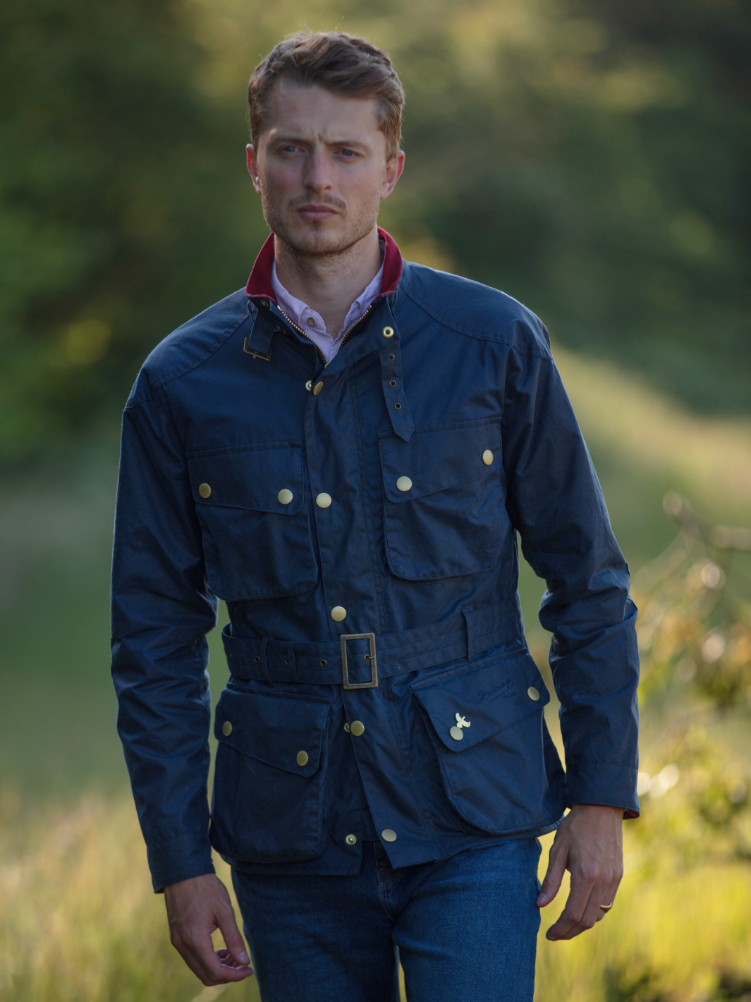 Men's Wax Biker Jacket in Ocean Navy with cherry check lining, burgundy cotton moleskin collar, oversized pockets, and detachable belt. Crafted from British waxed material with tonal embroidery and gold-coloured studs for a blend of tradition, luxury, and modern function.