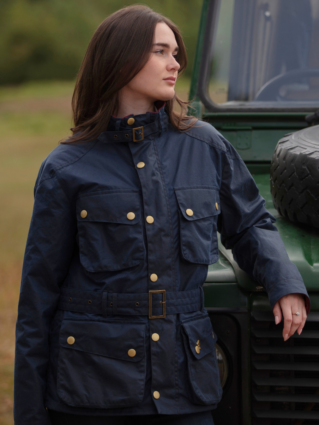 Wax Biker Jacket in Ocean Navy with cherry check lining, burgundy cotton moleskin collar, oversized pockets, and detachable belt. Crafted from British waxed material with tonal embroidery and gold-coloured studs for a blend of tradition, luxury, and modern function.
