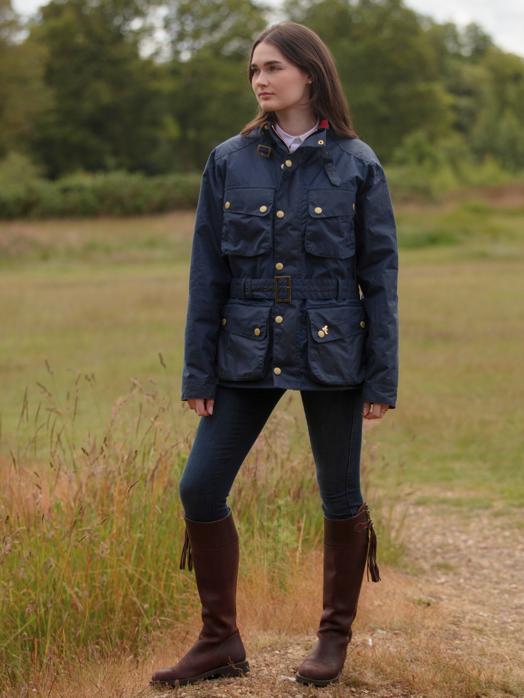 Wax Biker Jacket in Ocean Navy with cherry check lining, burgundy cotton moleskin collar, oversized pockets, and detachable belt. Crafted from British waxed material with tonal embroidery and gold-coloured studs for a blend of tradition, luxury, and modern function.
