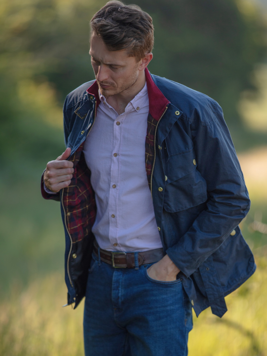 Men's Wax Biker Jacket in Ocean Navy with cherry check lining, burgundy cotton moleskin collar, oversized pockets, and detachable belt. Crafted from British waxed material with tonal embroidery and gold-coloured studs for a blend of tradition, luxury, and modern function.