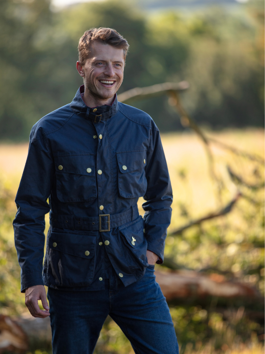 Men's Wax Biker Jacket in Ocean Navy with cherry check lining, burgundy cotton moleskin collar, oversized pockets, and detachable belt. Crafted from British waxed material with tonal embroidery and gold-coloured studs for a blend of tradition, luxury, and modern function.