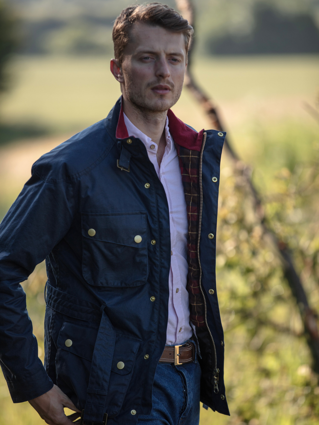 Men's Wax Biker Jacket in Ocean Navy with cherry check lining, burgundy cotton moleskin collar, oversized pockets, and detachable belt. Crafted from British waxed material with tonal embroidery and gold-coloured studs for a blend of tradition, luxury, and modern function.