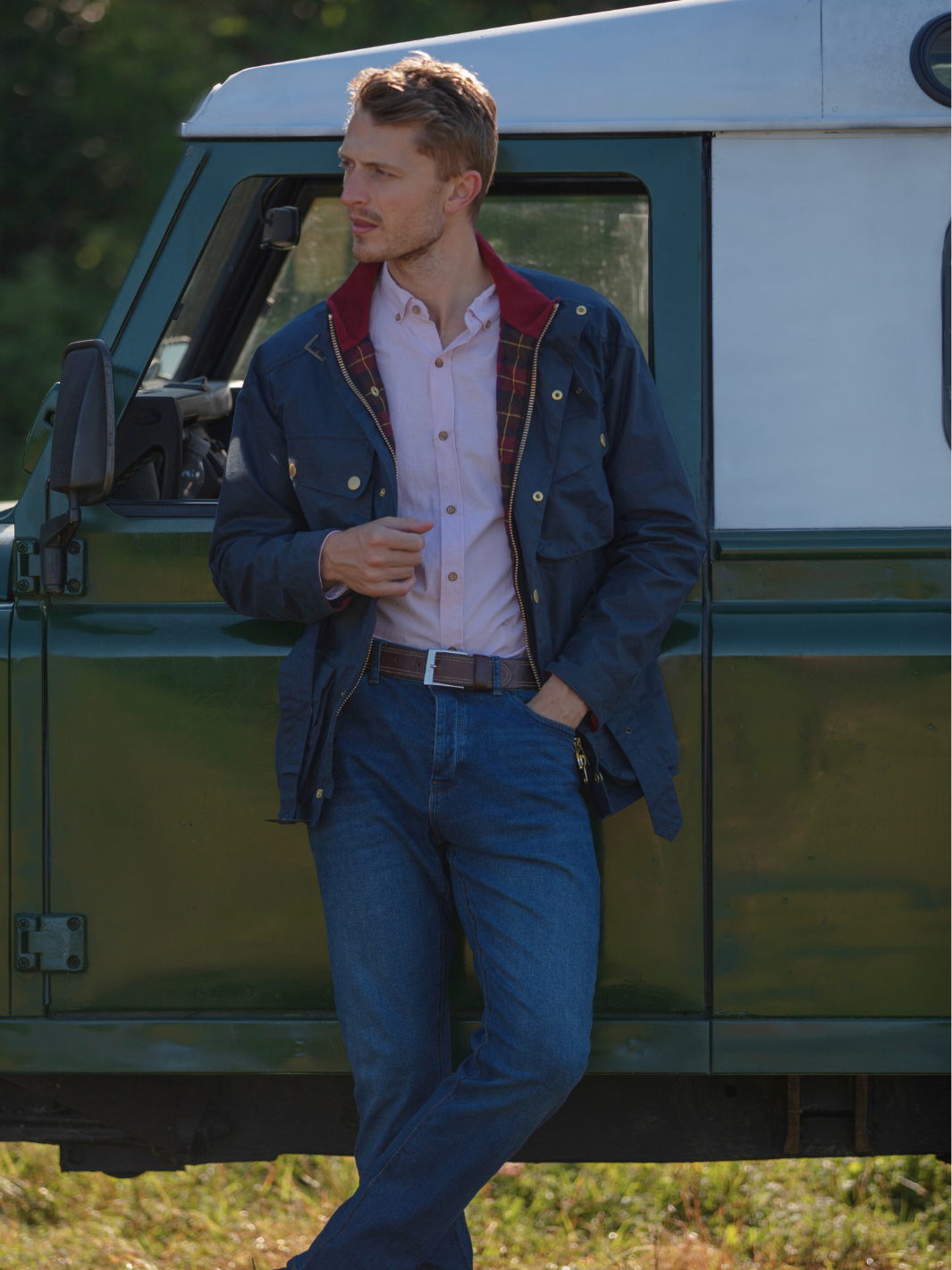 Men's Wax Biker Jacket in Ocean Navy with cherry check lining, burgundy cotton moleskin collar, oversized pockets, and detachable belt. Crafted from British waxed material with tonal embroidery and gold-coloured studs for a blend of tradition, luxury, and modern function.