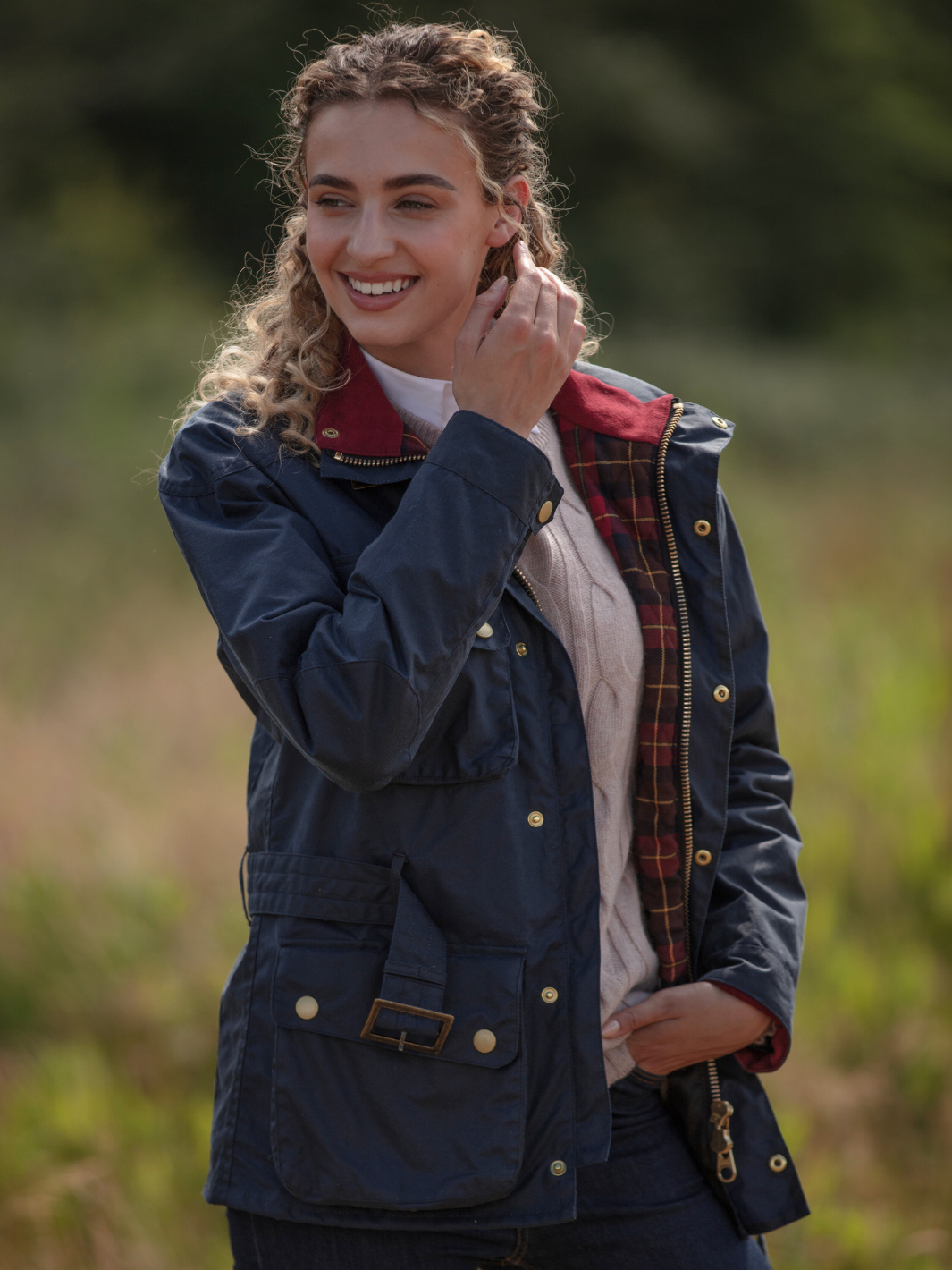 Wax Biker Jacket in Ocean Navy with cherry check lining, burgundy cotton moleskin collar, oversized pockets, and detachable belt. Crafted from British waxed material with tonal embroidery and gold-coloured studs for a blend of tradition, luxury, and modern function.