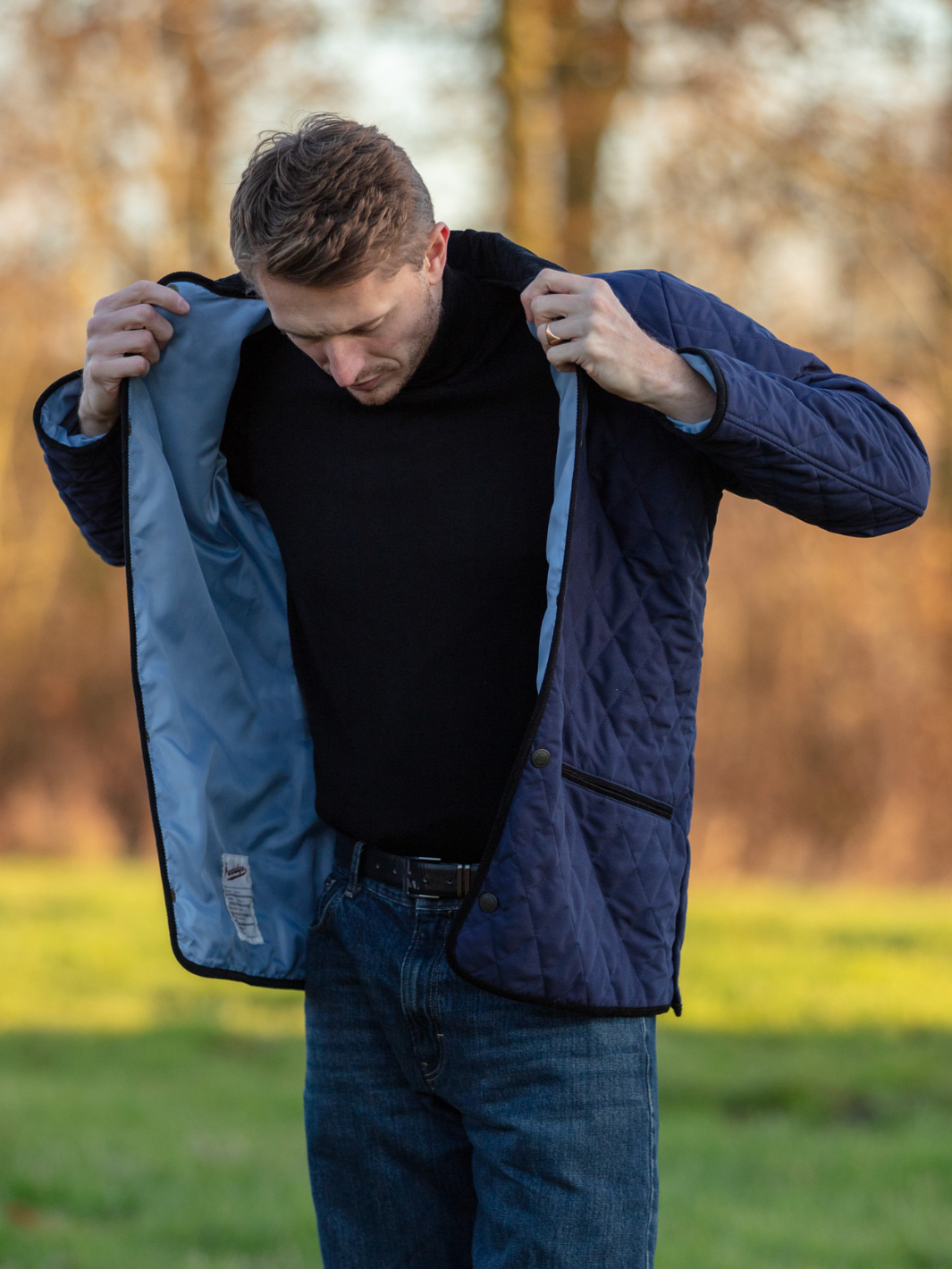 Men’s Quilted Jacket | Navy quilted jacket with light blue lining, black roll-neck jumper and blue jeans